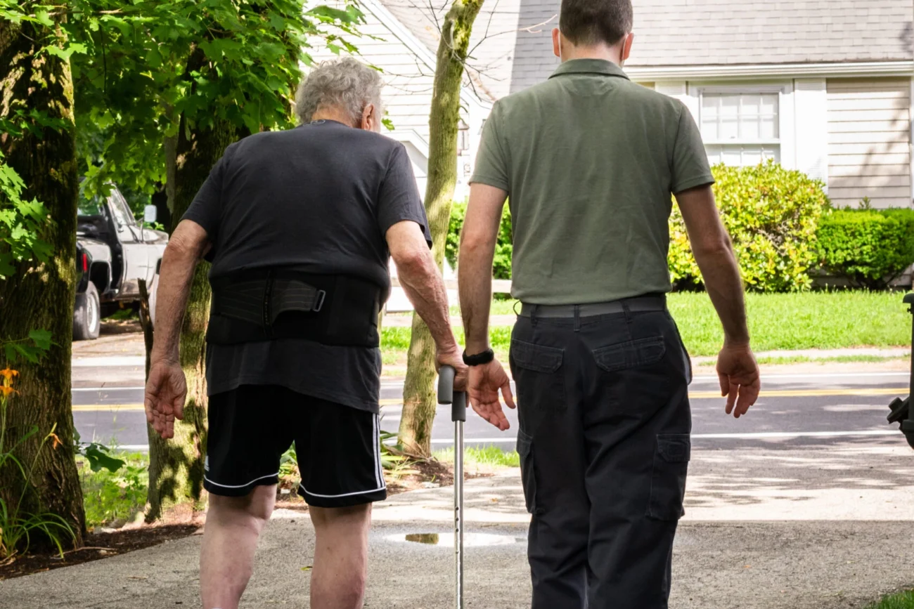 A caregiver walking beside a patient using a cane